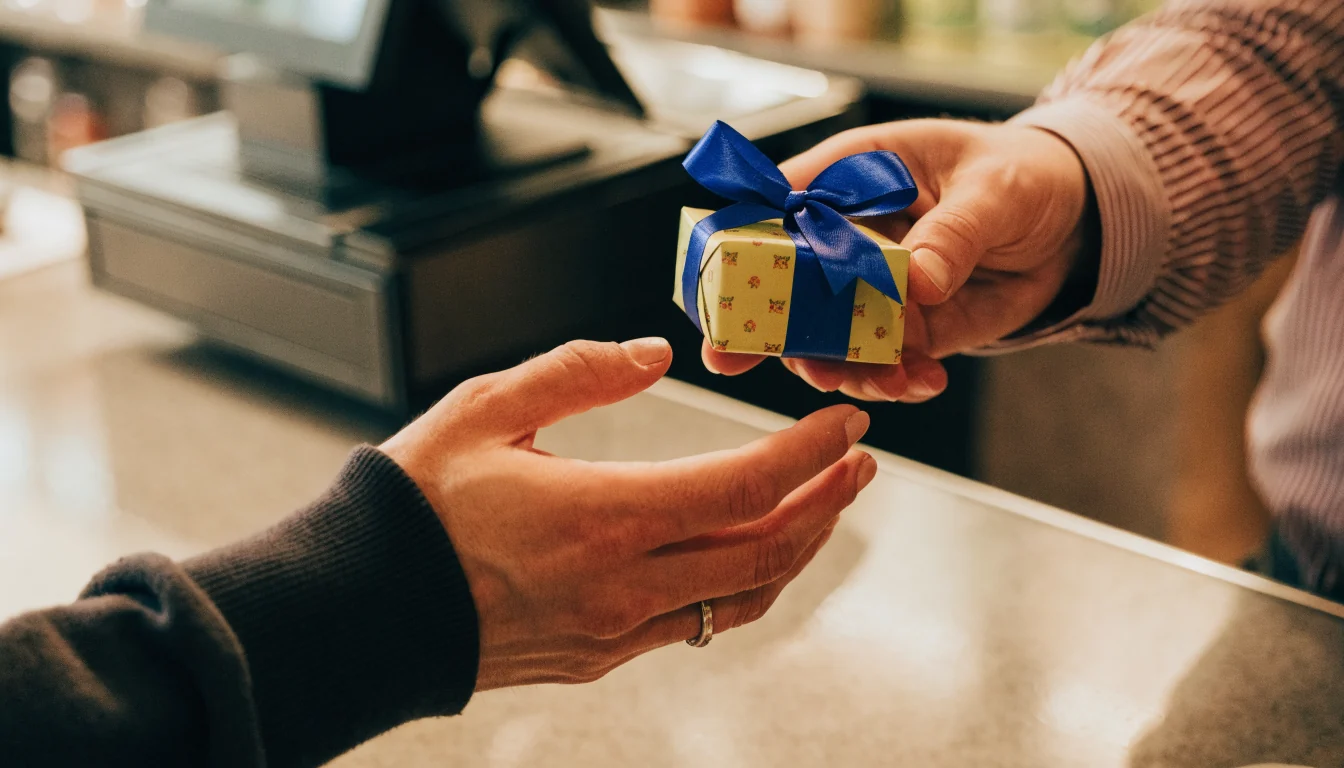 Hands passing a gift box with a vivid ribbon across a cafe counter